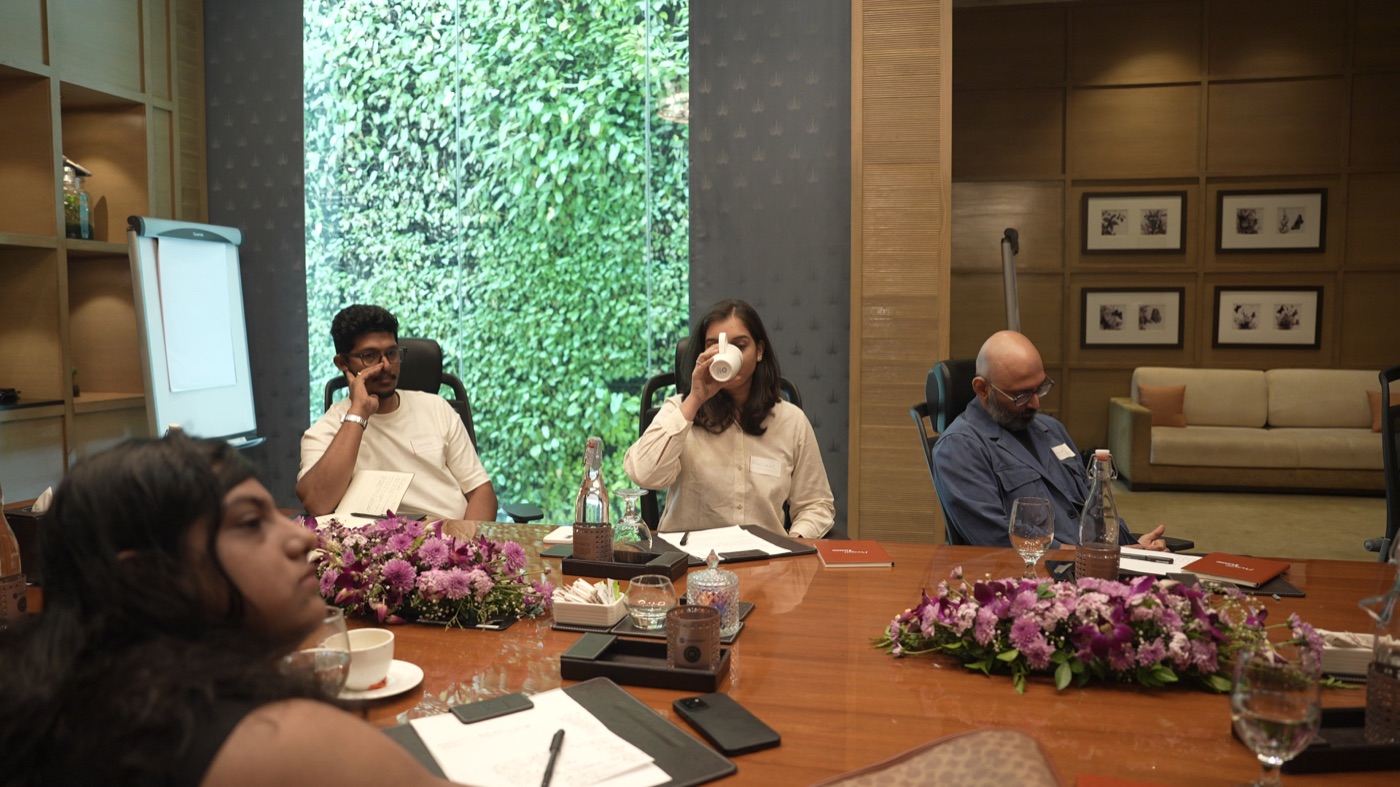 Participants seated around the table, one pausing over a cup of coffee.