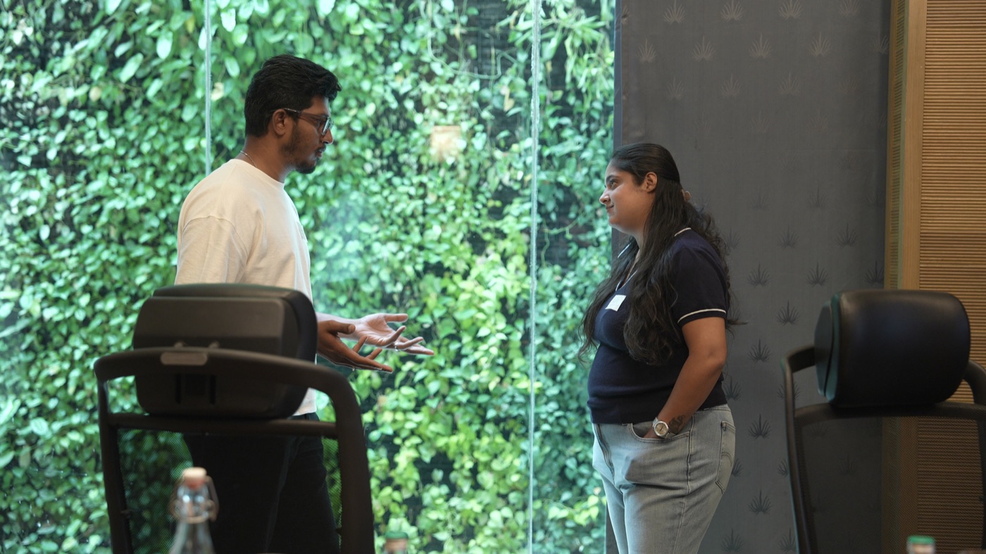 Two participants standing in conversation by the green wall.