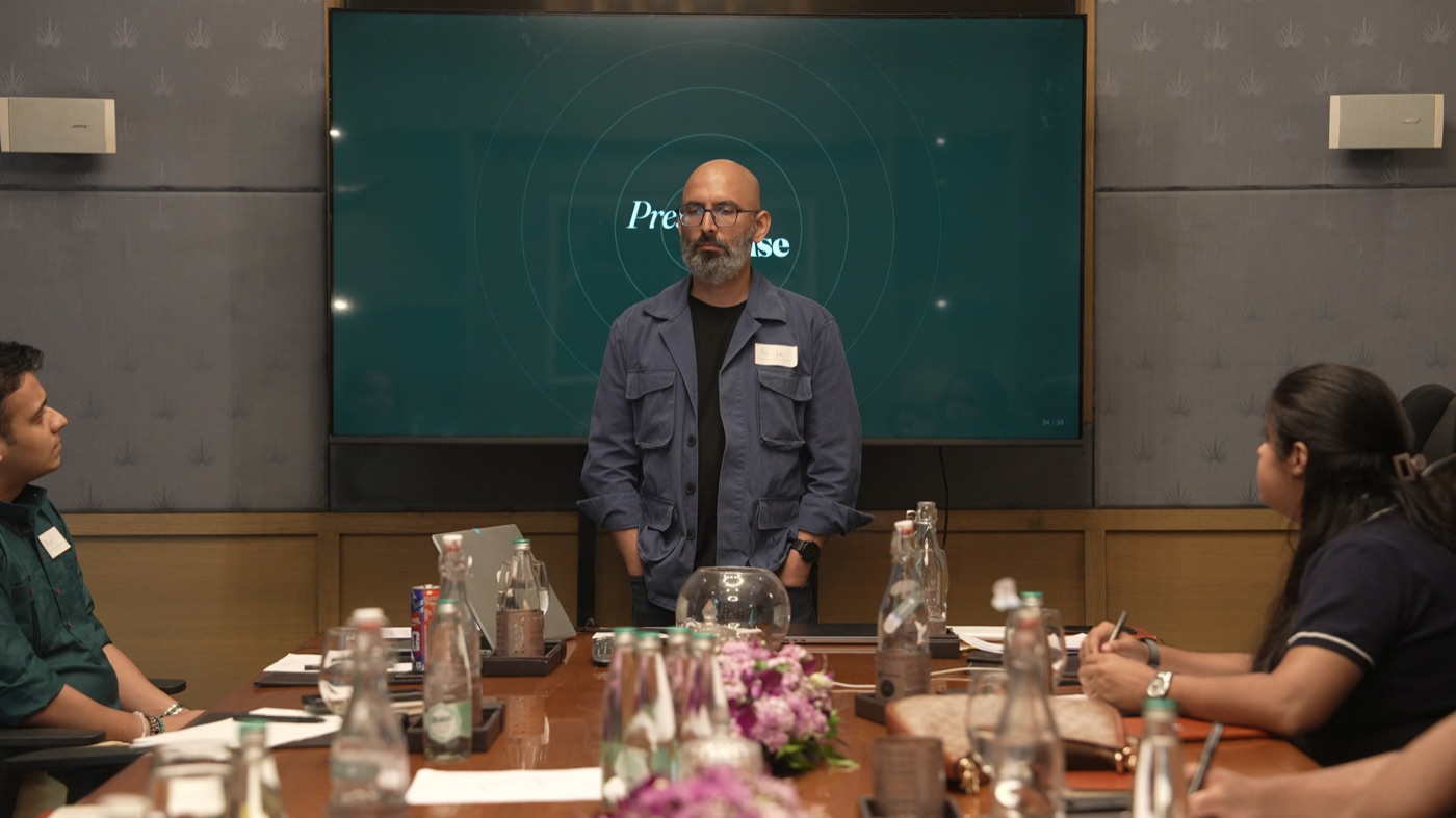 A participant standing at the head of the table, the Present Tense screen behind.