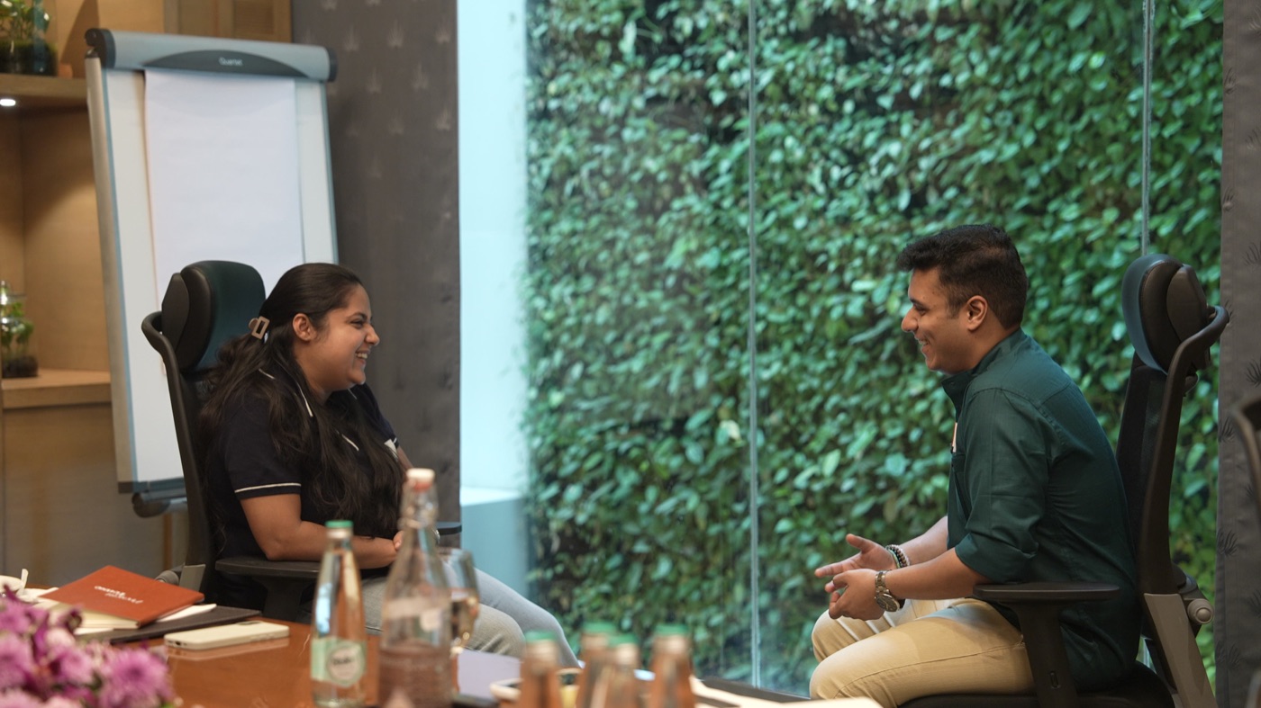 Two participants seated by the green wall, laughing mid-conversation.