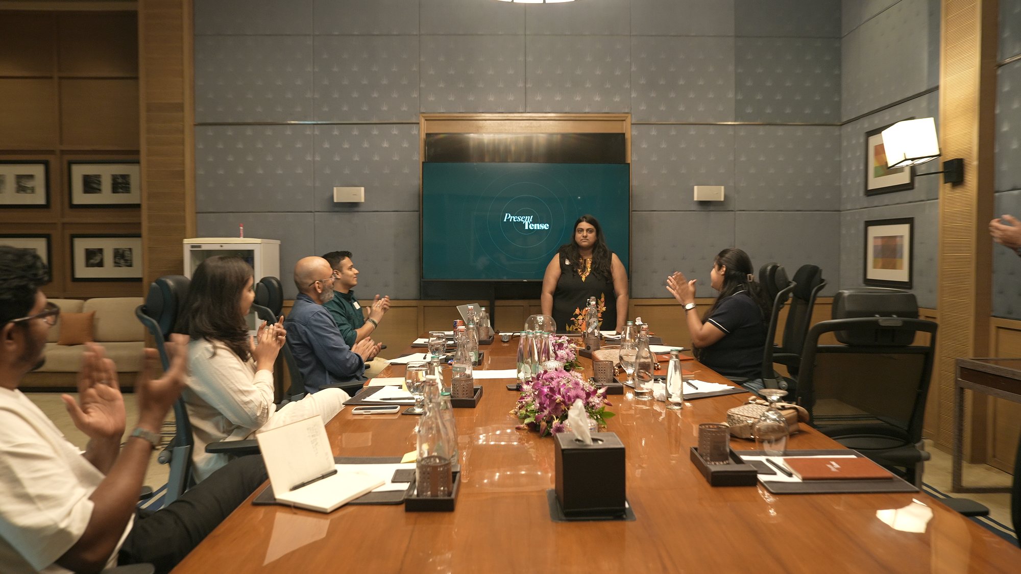 The room applauds a participant standing at the Present Tense screen.