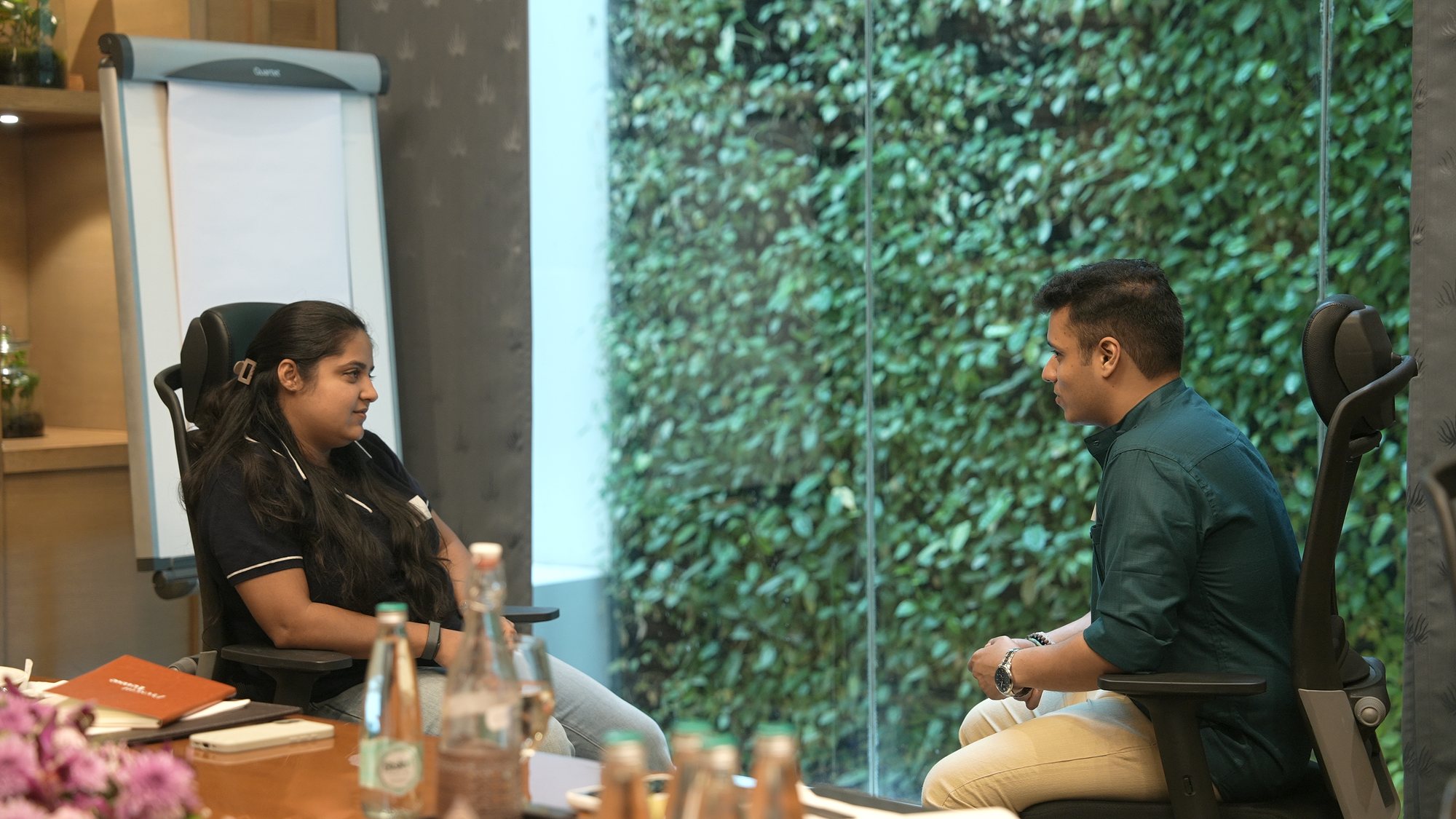 A participant and Yash seated by the green wall, mid-conversation.
