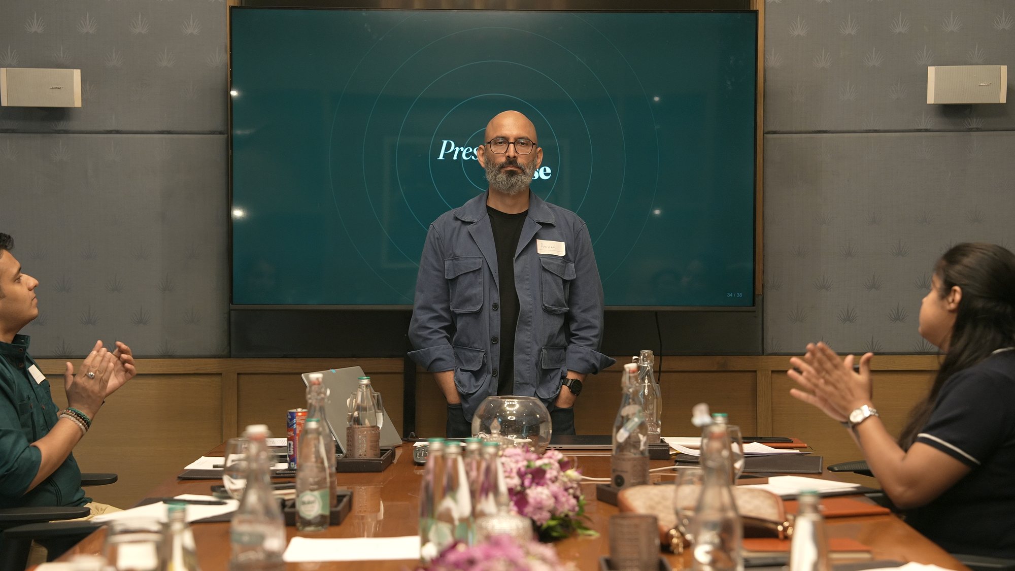 A participant standing at the Present Tense screen while the table applauds.