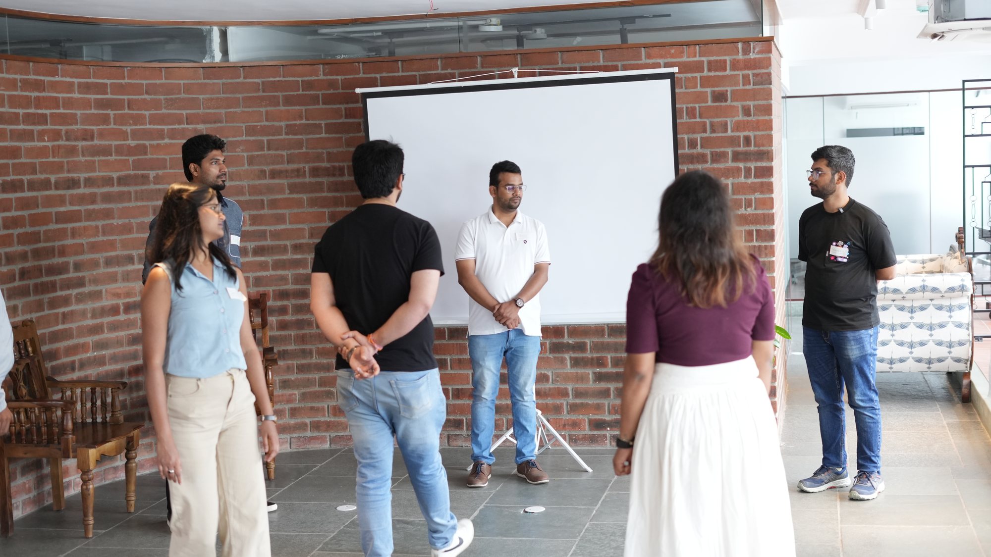 Participants mid-exercise in Go, standing in a loose circle in front of the Present Tense screen.