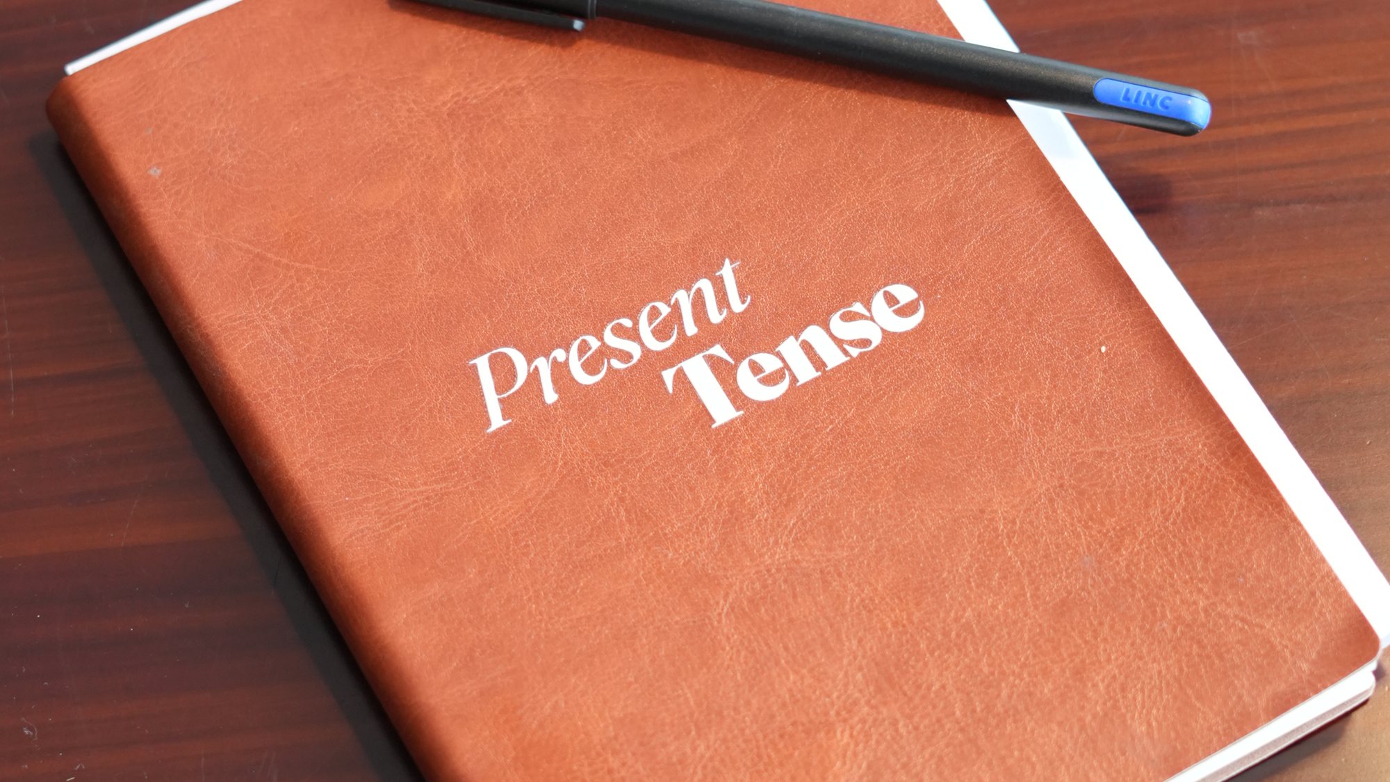 A Present Tense notebook and pen on a wooden table.