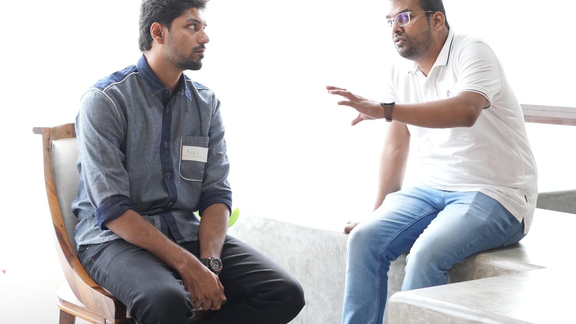 Two participants in conversation by the window, one gesturing as he speaks.