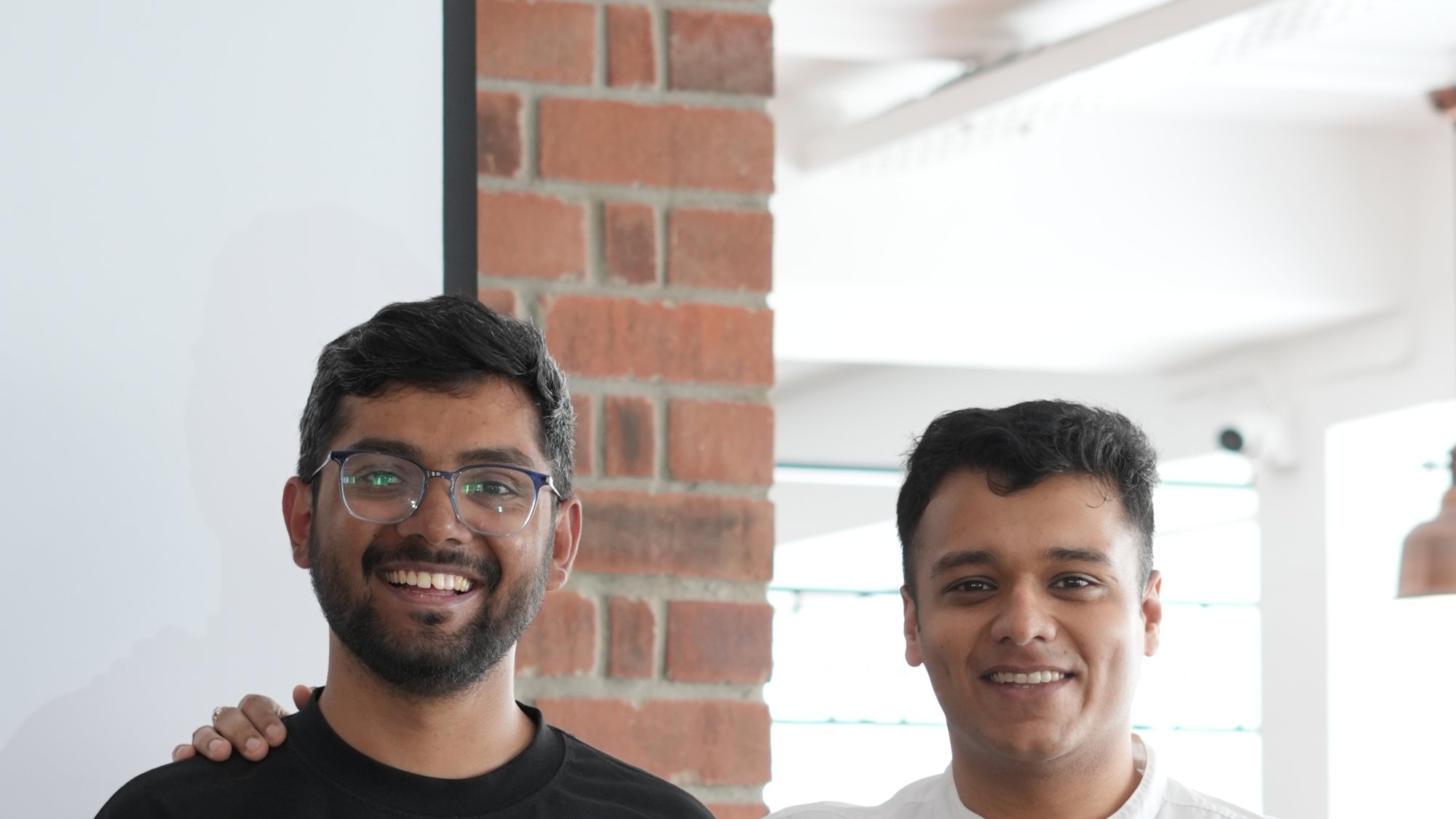 Praveen and Yash, the two hosts, against the brick wall.